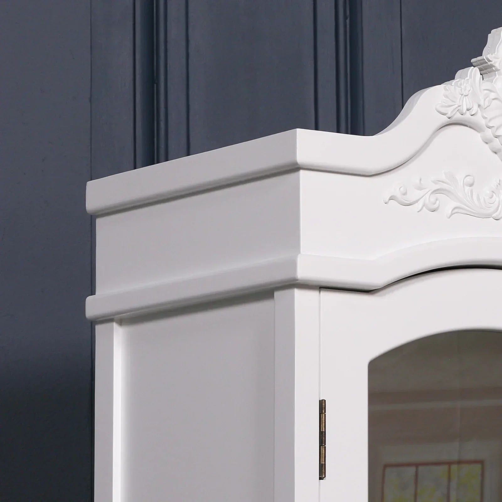White wooden wardrobe top with ornate detailing against dark paneled wall