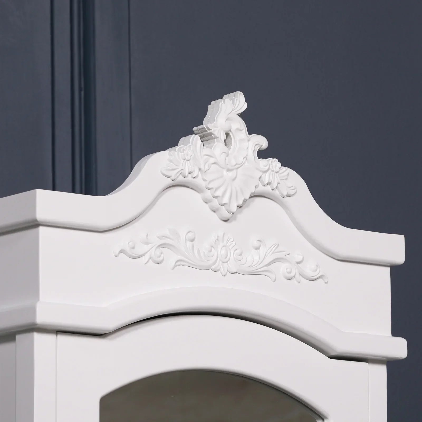 White ornate wardrobe top with decorative floral carvings against dark wall