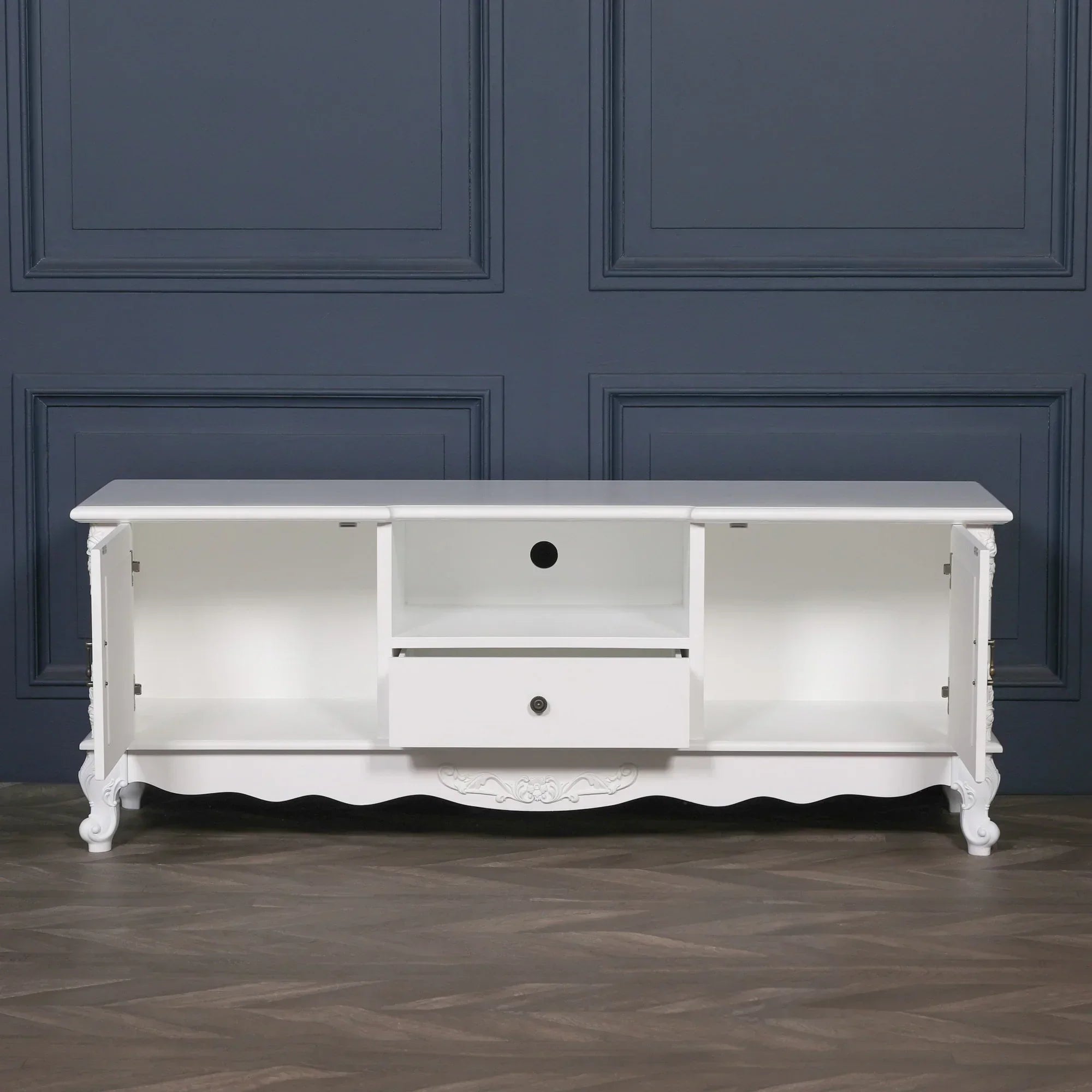 White wooden TV unit with two open cabinets, central shelf and single drawer, ornate base