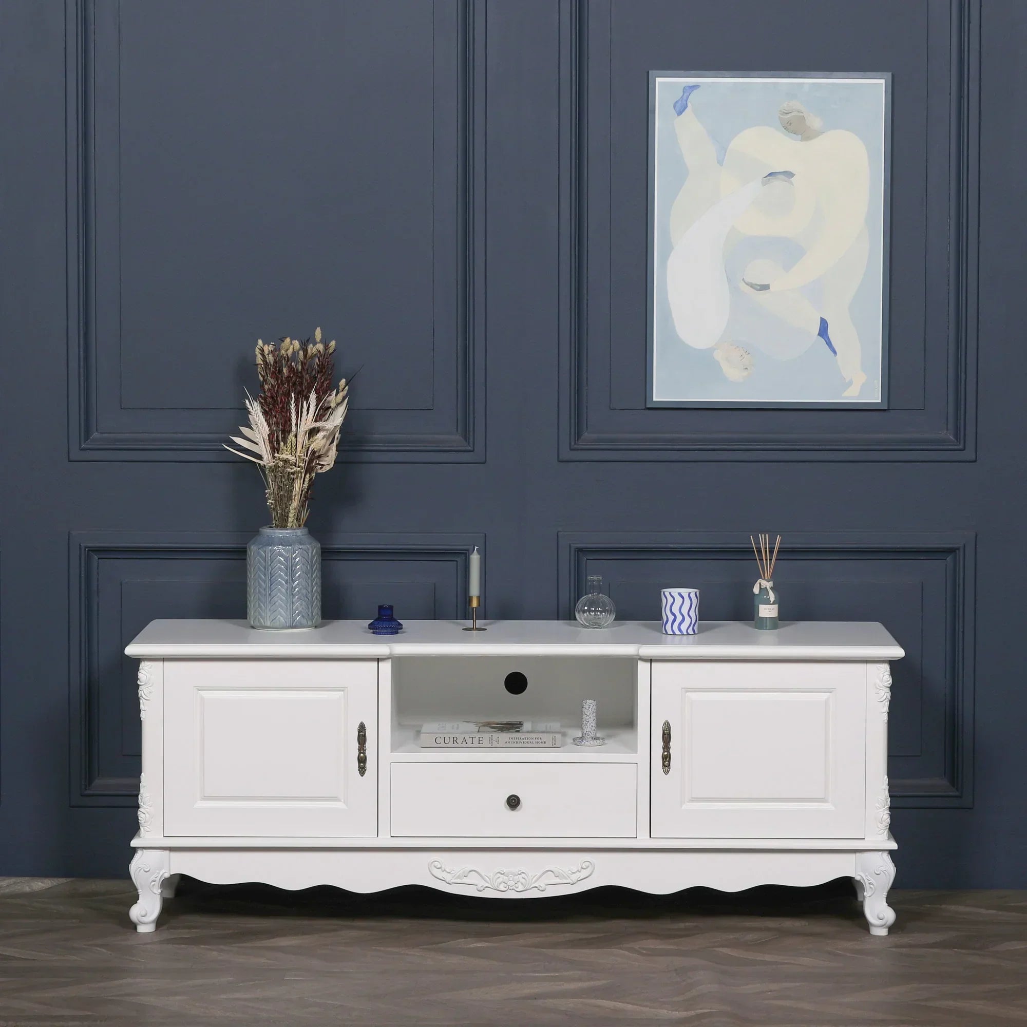 White wooden TV unit with two cabinets, central drawer and shelving, styled in modern living room