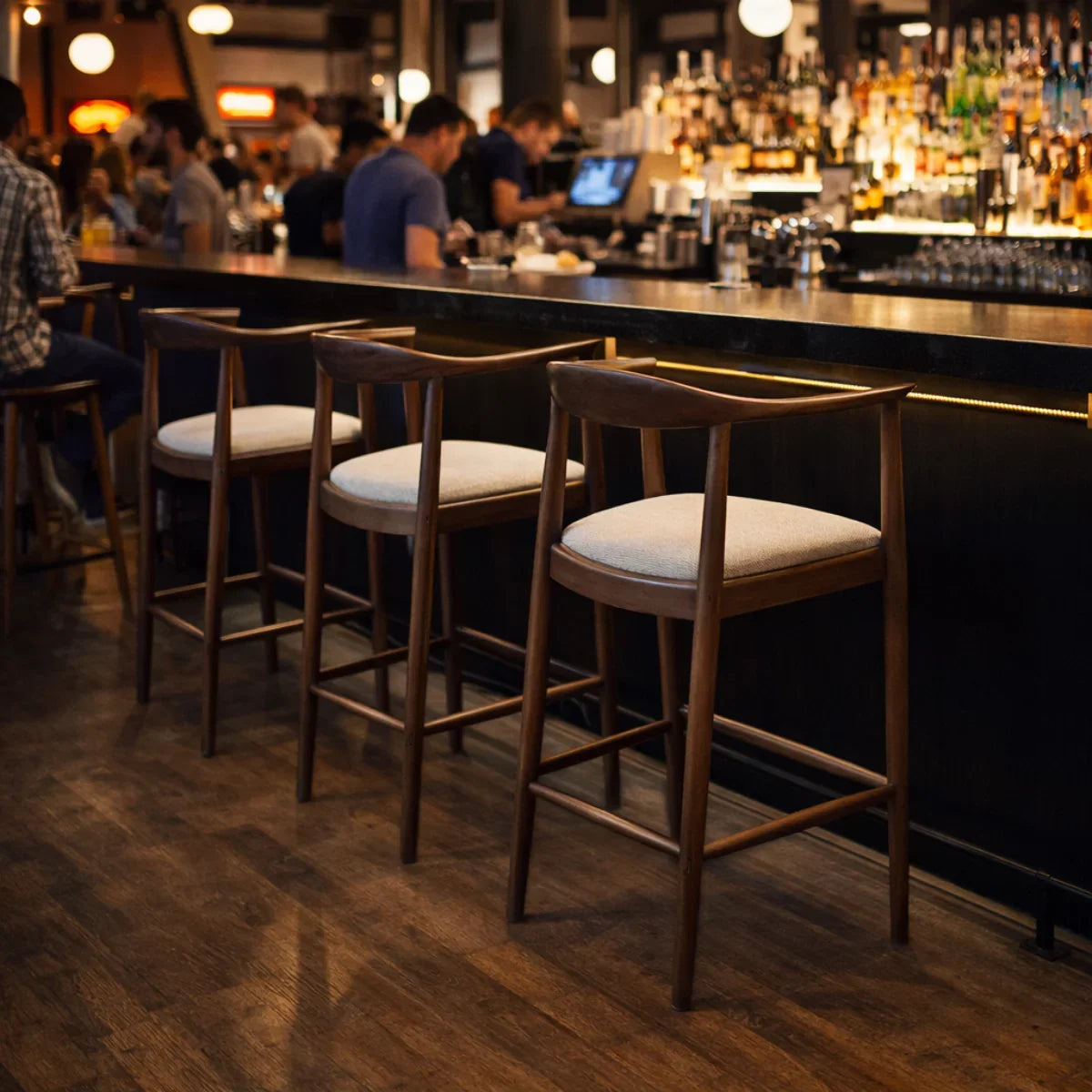 Fern barstool with wood frame and padded seat at a bar counter in a lively setting
