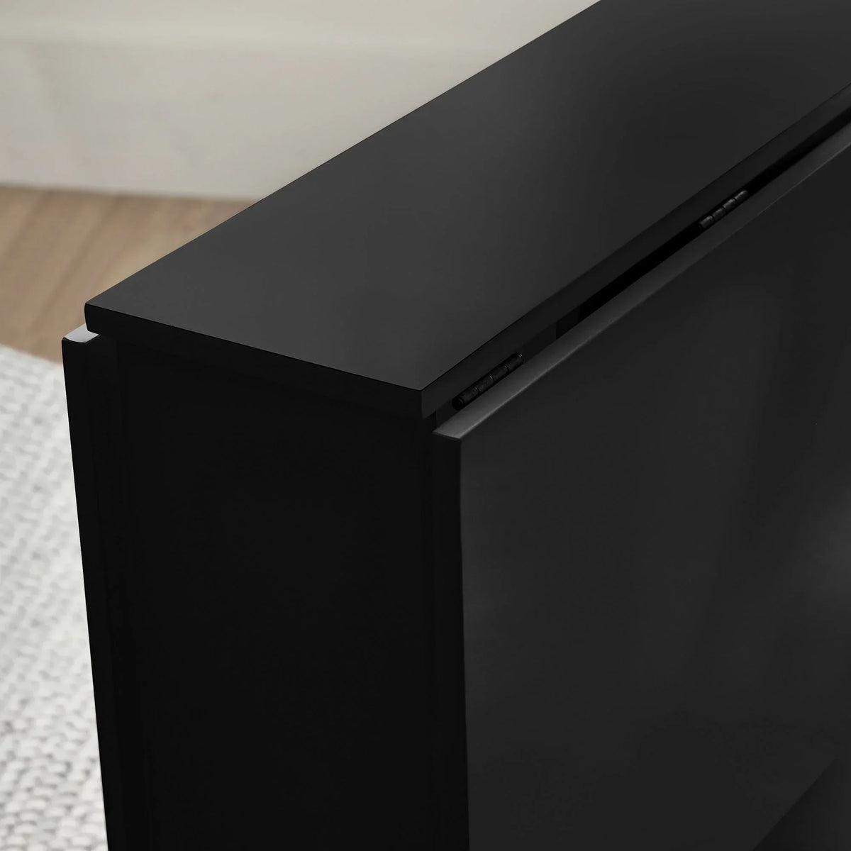 Black gateleg table corner detail showing smooth wood surface and folding hinge