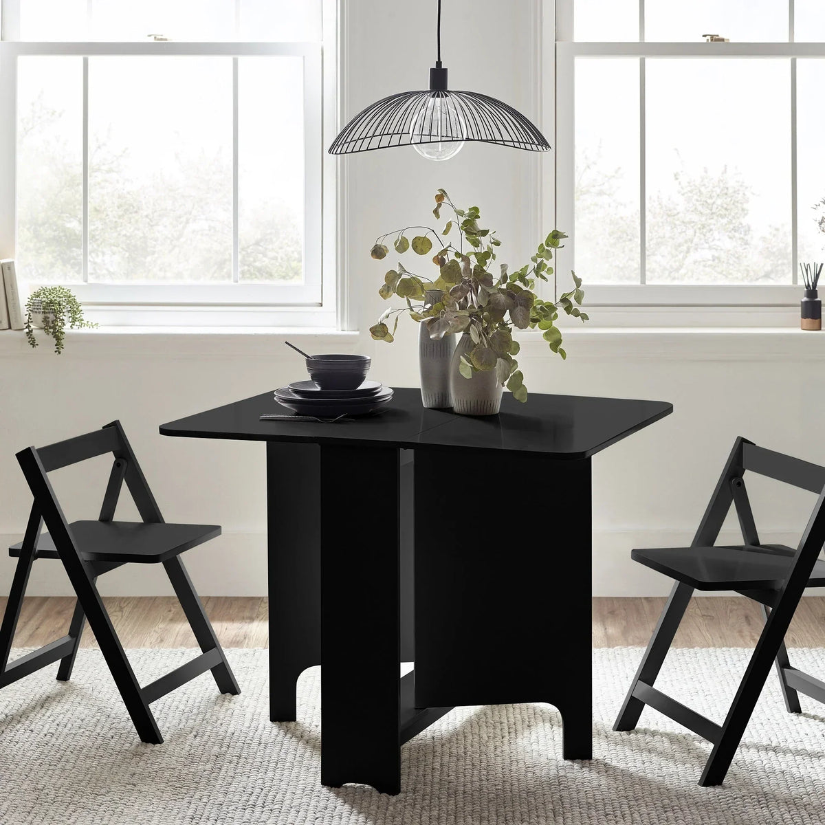 Black gateleg dining table with two matching folding chairs in a bright room