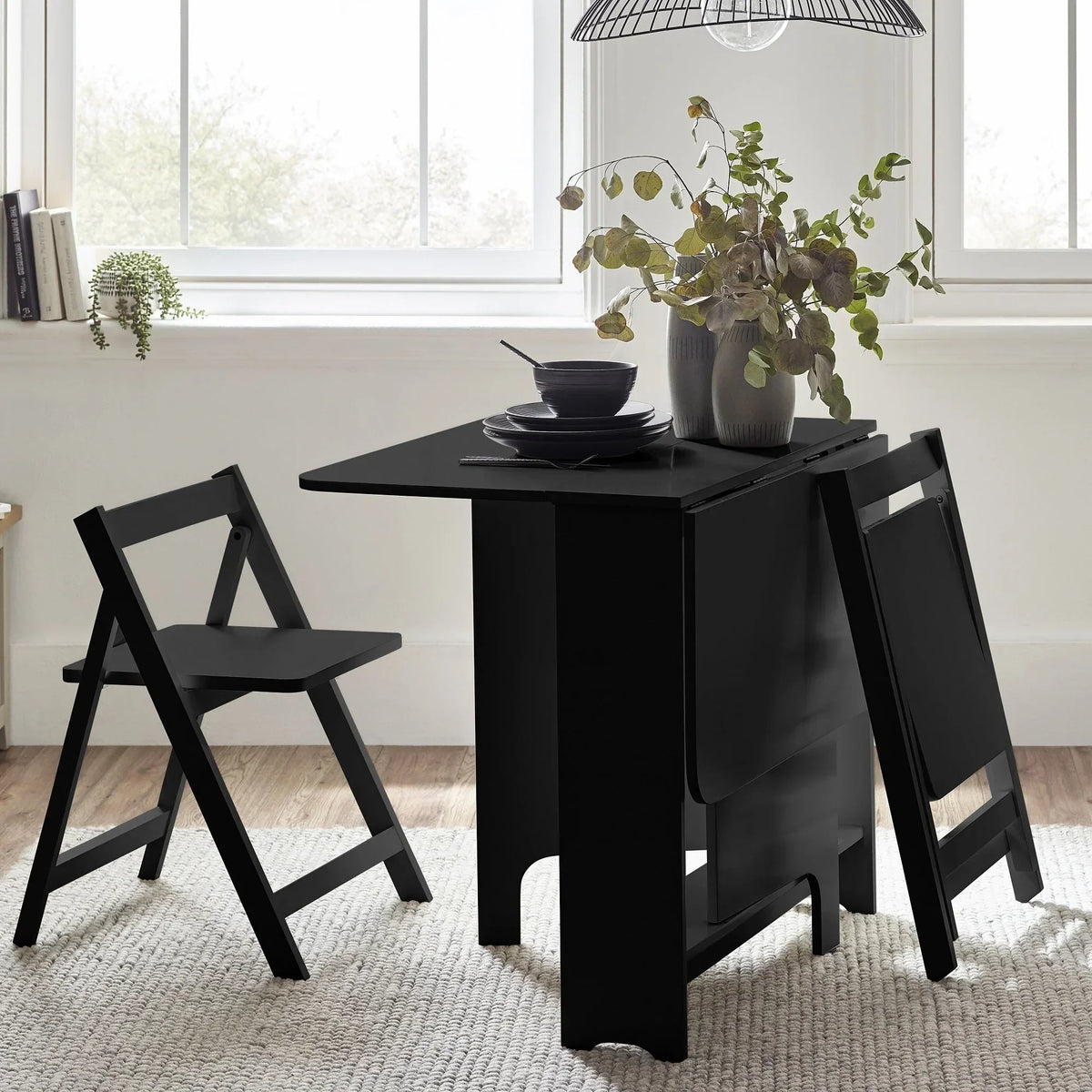 Black gateleg dining table with two folding chairs in bright modern room