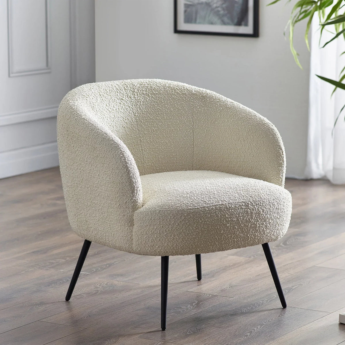 Cream boucle accent chair with curved back and black legs on wooden floor in modern room