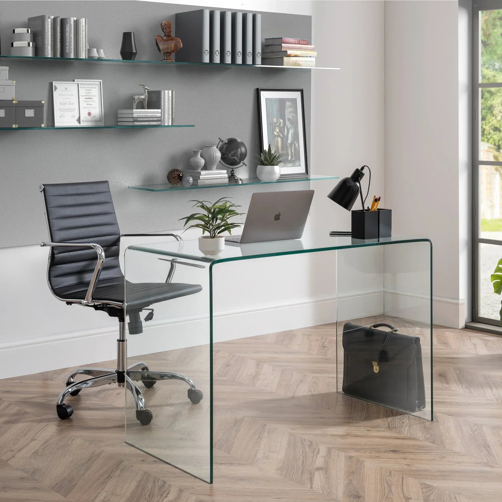Black office chair with chrome frame beside glass desk in modern home office setting