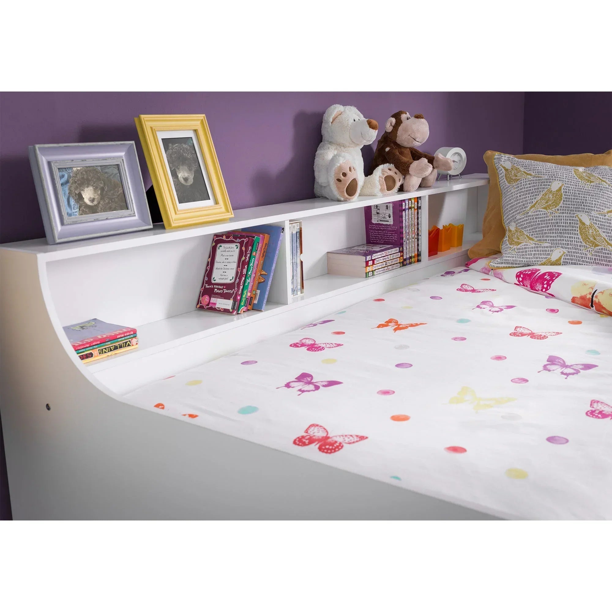 White daybed with bookshelf headboard, children's bedding, toys, books, and picture frames