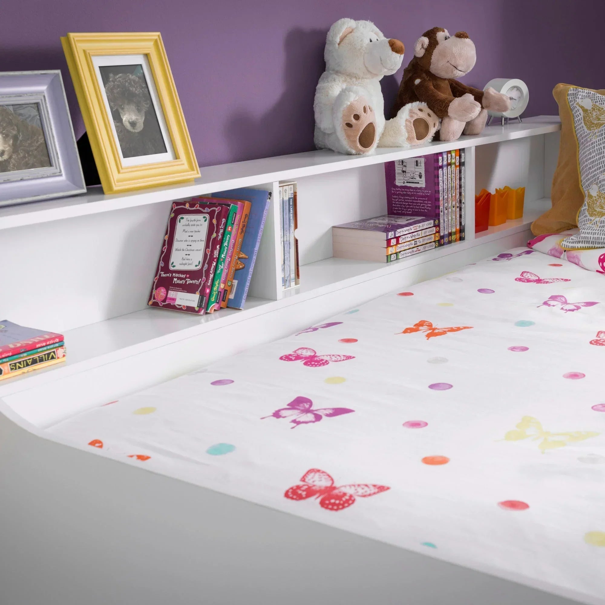 White daybed with built-in shelf, books, toys, and butterfly print bedding against purple wall