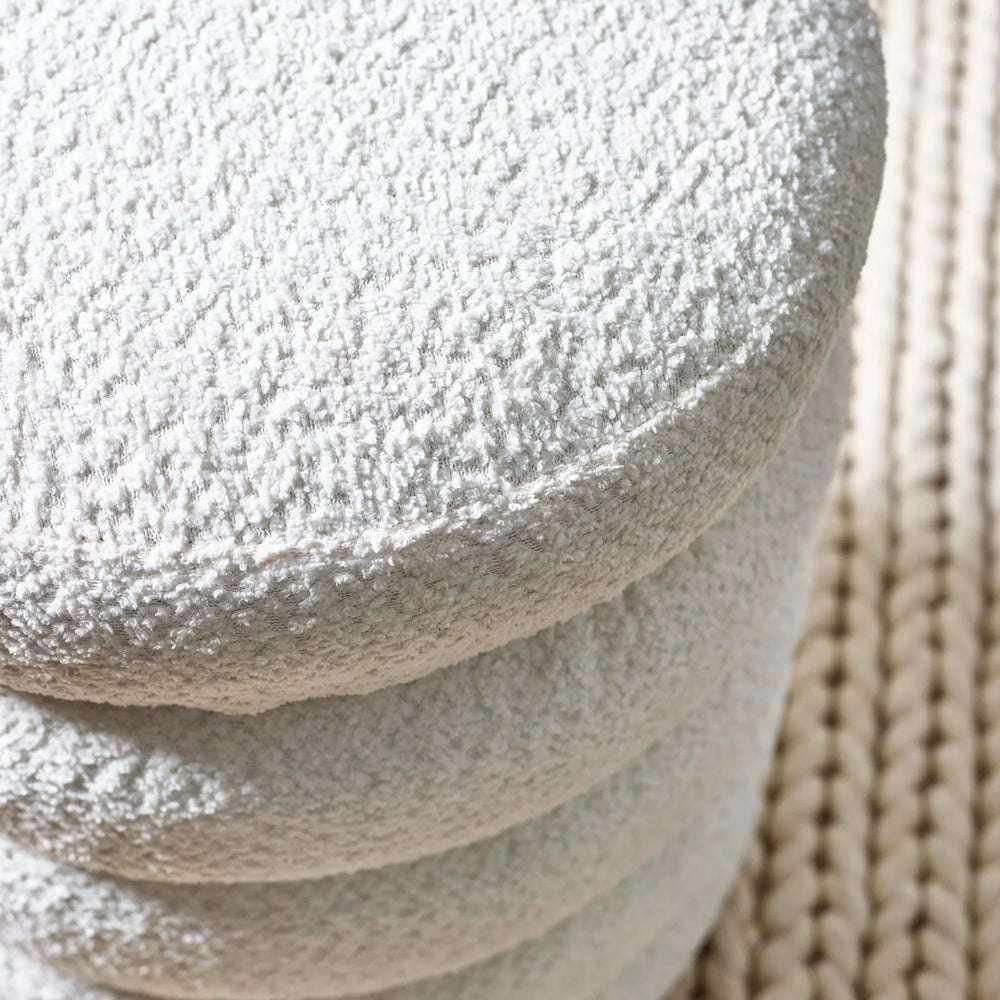 Round cream bouclé stool detail with textured upholstery on woven rug