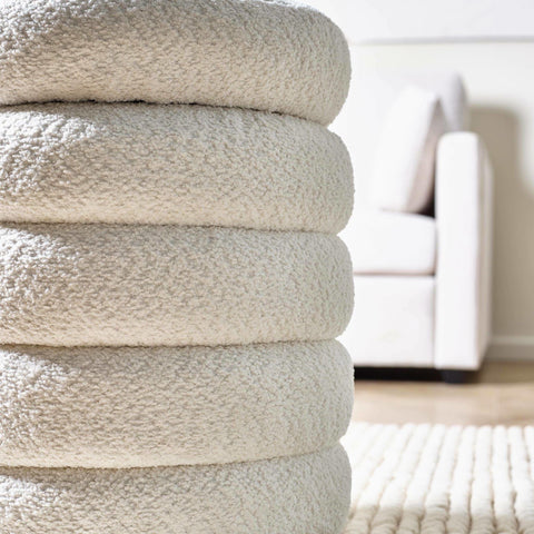 Ivory boucle upholstered ottoman stacked beside cream sofa on textured rug