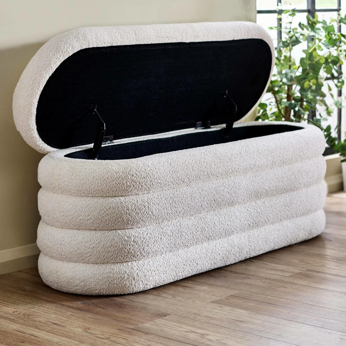 Cream bouclé storage bench with open lid on wood floor near window