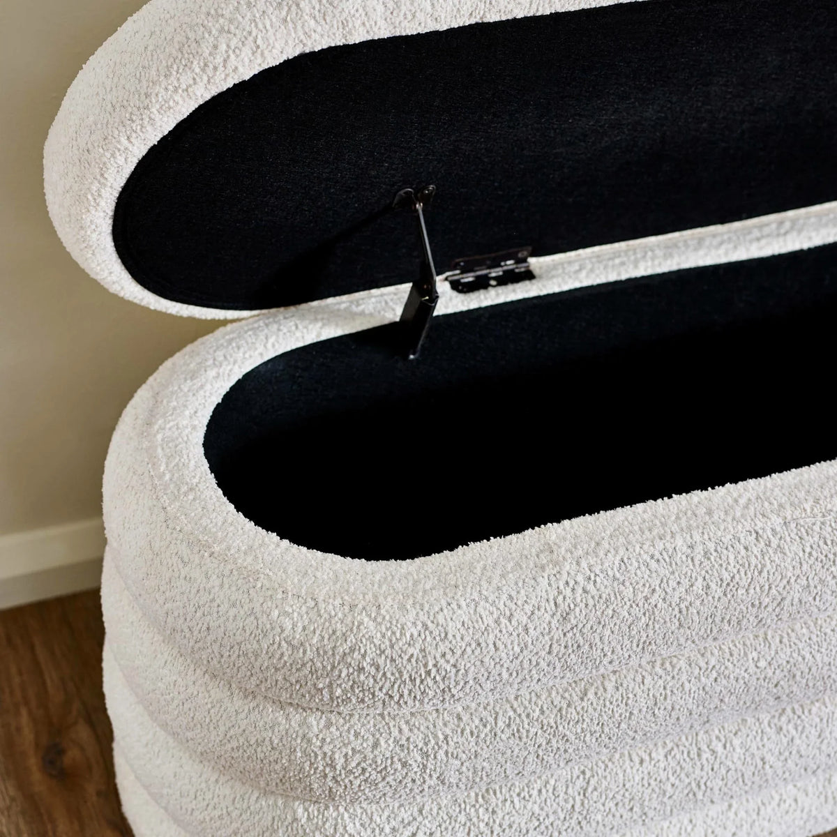 Textured white storage ottoman with open hinged lid and black interior on wooden floor
