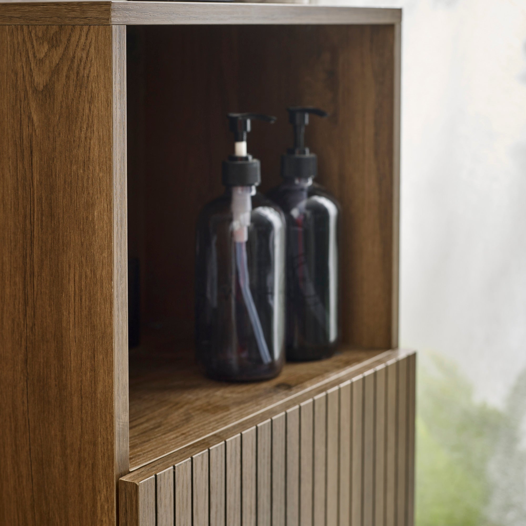Close-up of brown wooden cabinet with two black pump bottles in open upper shelf.