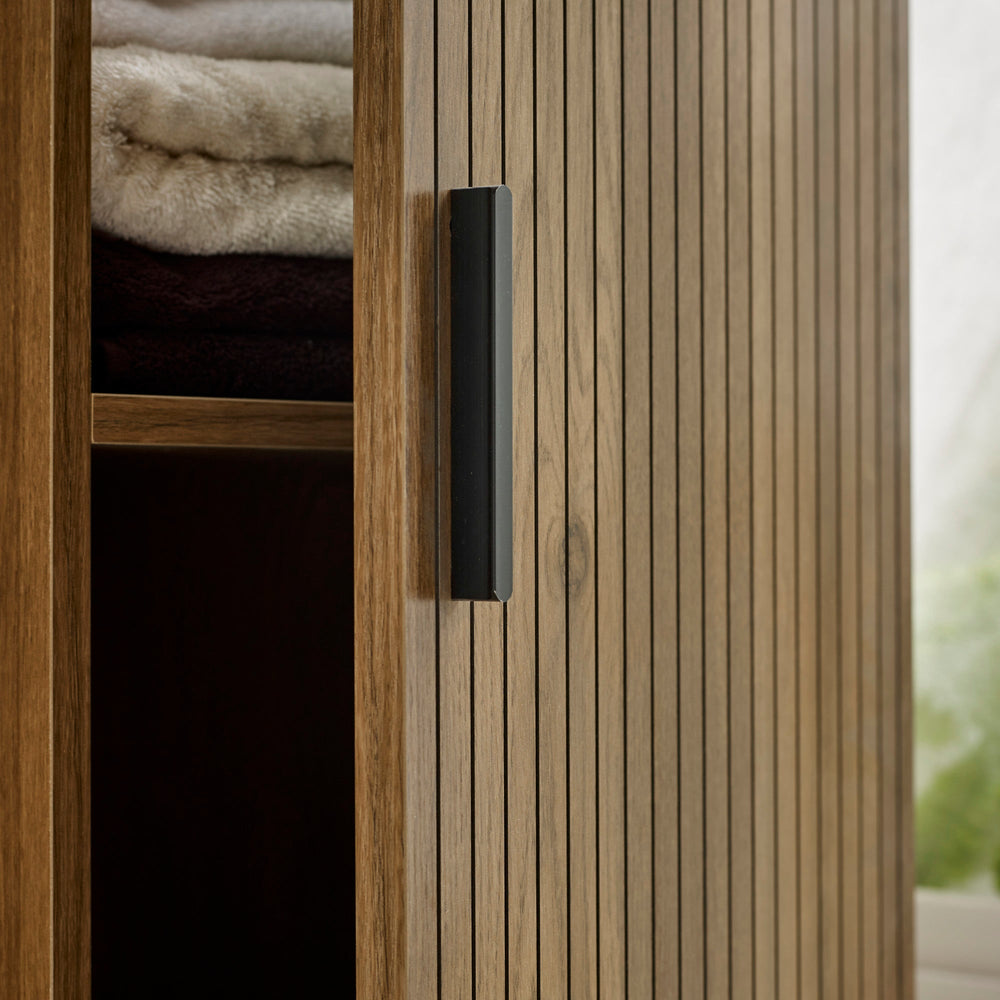 Detail of cabinet door with vertical grooves and black handle, partially opened with towels inside.