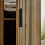 Detail of cabinet door with vertical grooves and black handle, partially opened with towels inside.
