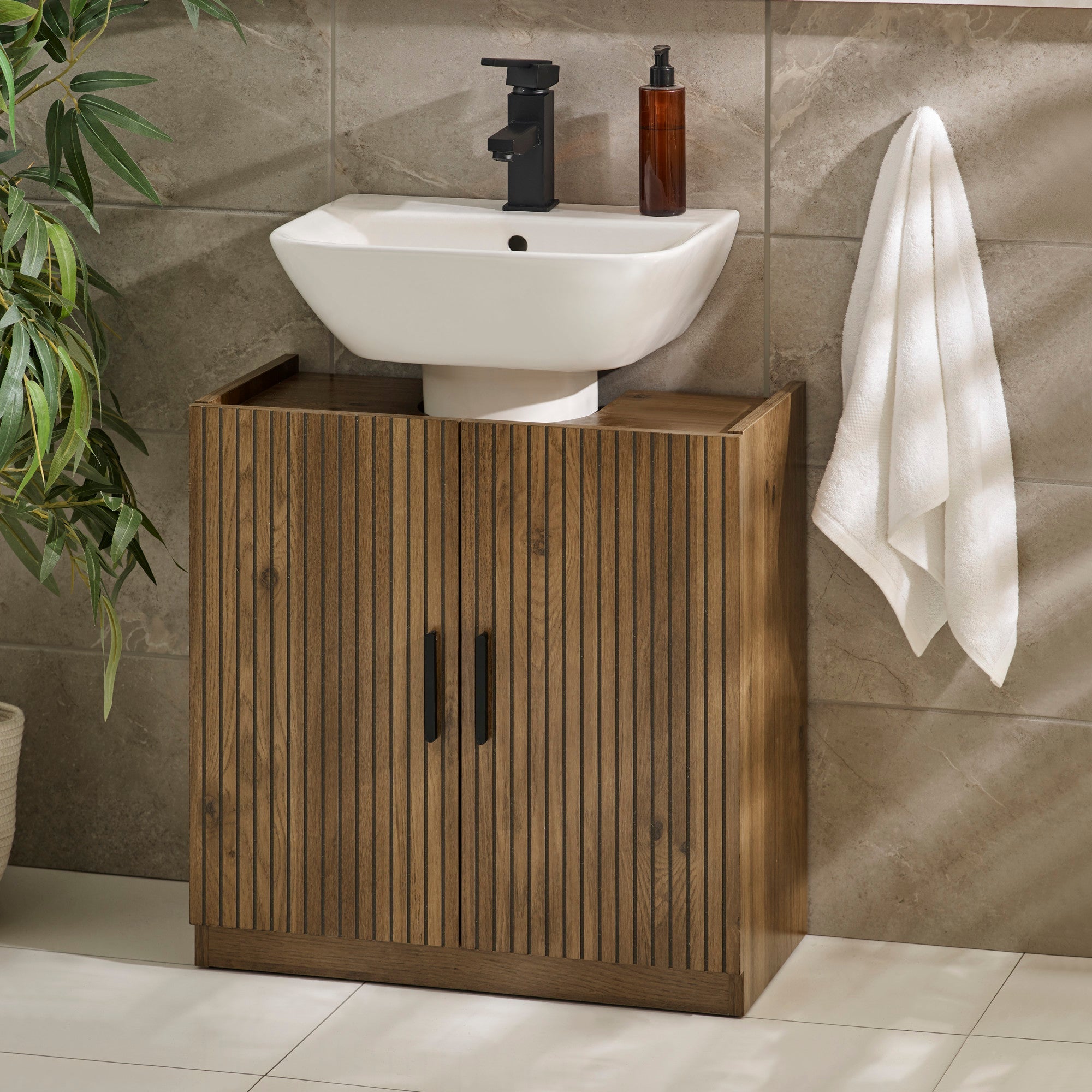 Wooden under sink bathroom storage unit with vertical grooves and black handles in tiled room