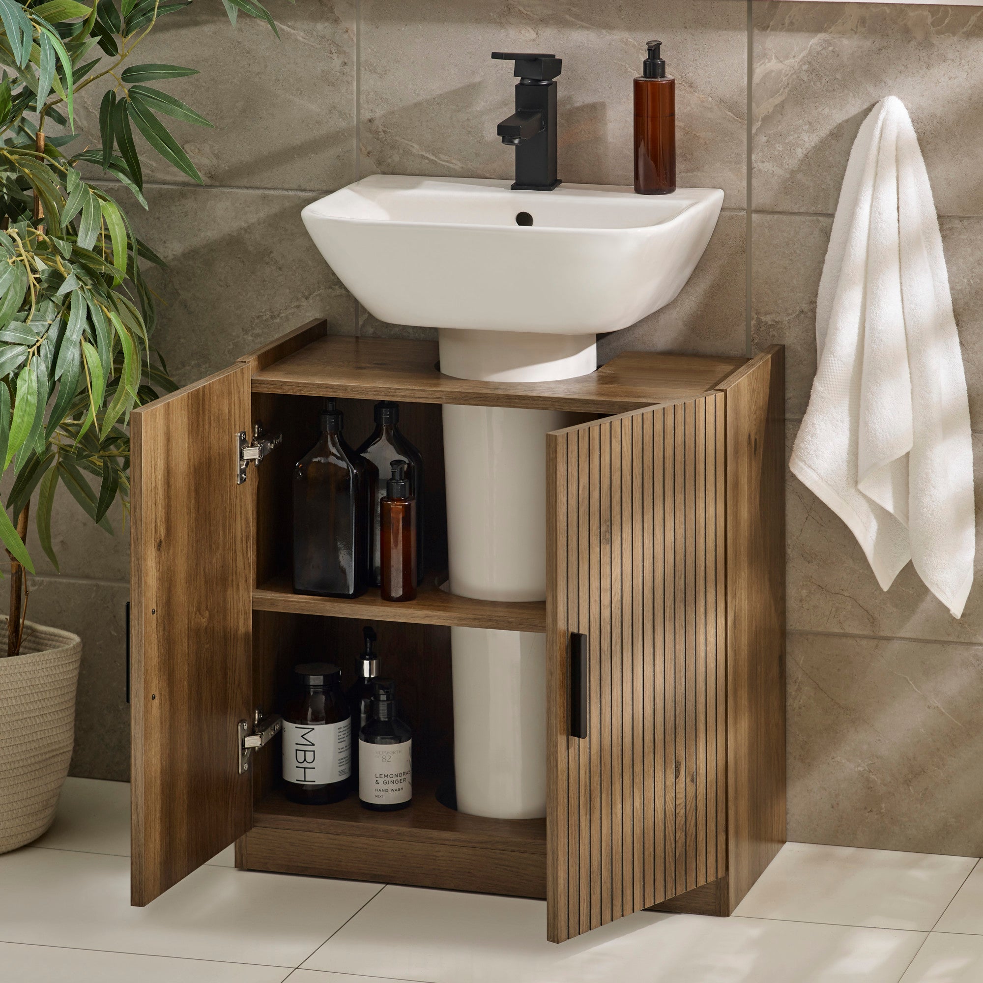 Open two-door wooden under sink bathroom unit showing two shelves with toiletries inside