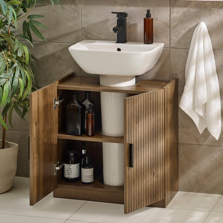 Open two-door wooden under sink bathroom unit showing two shelves with toiletries inside