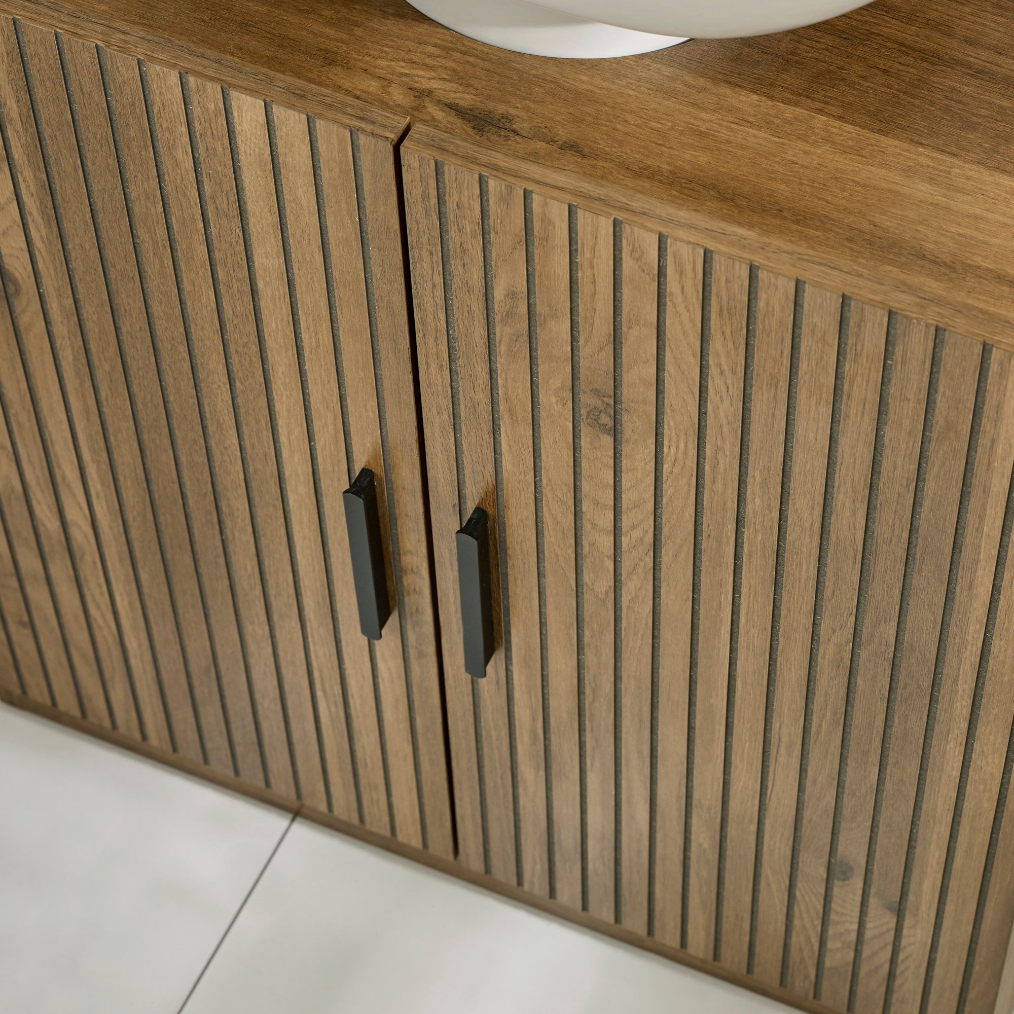 Close-up of closed doors on wooden bathroom storage unit showing vertical groove pattern and black handles