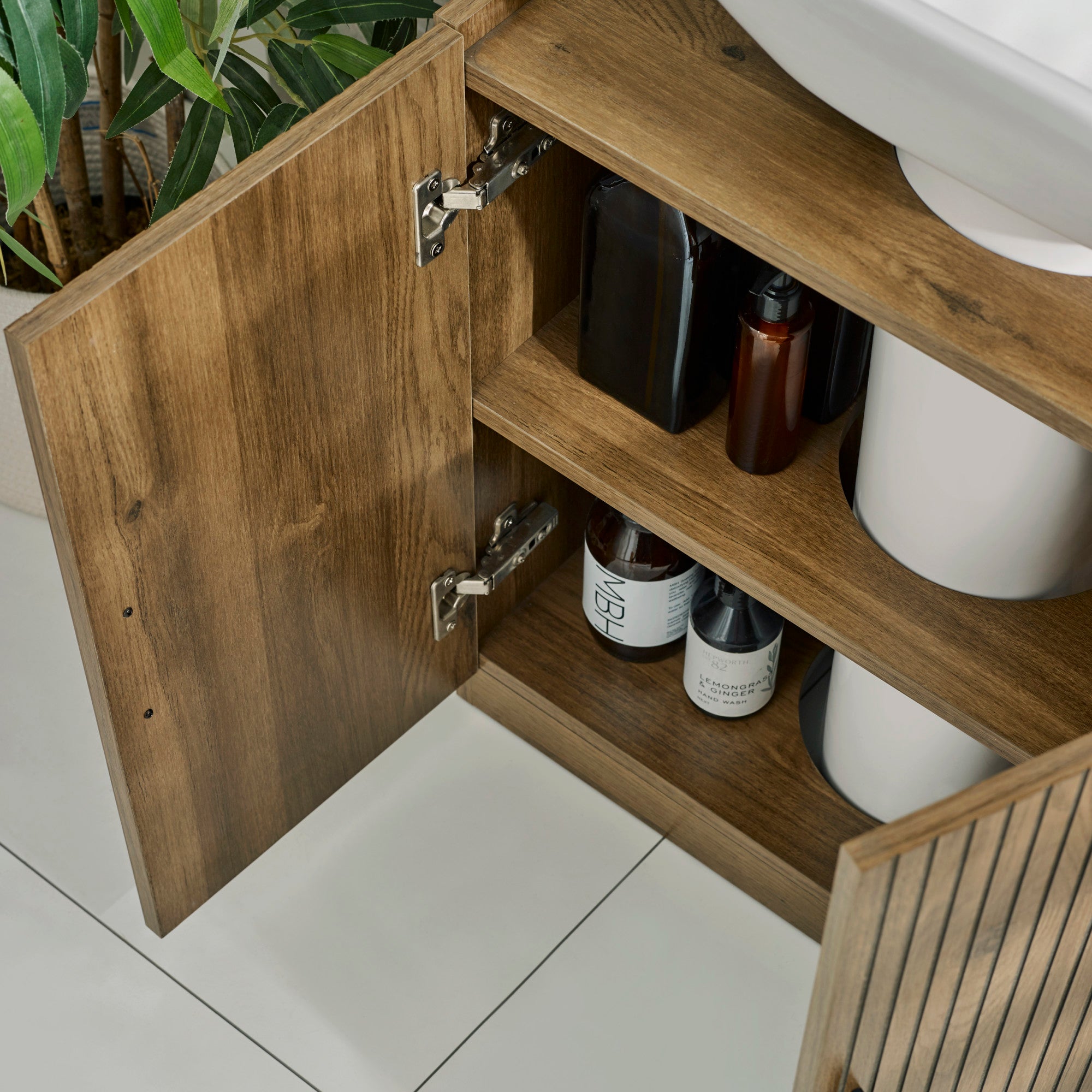 Under sink bathroom unit in brown wood with vertical grooves and black pull handles close-up