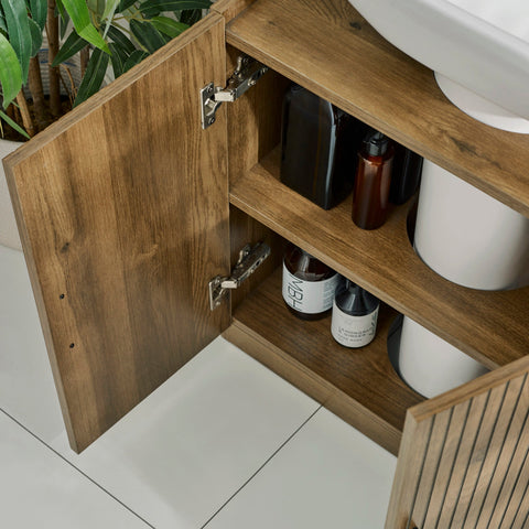 Under sink bathroom unit in brown wood with vertical grooves and black pull handles close-up
