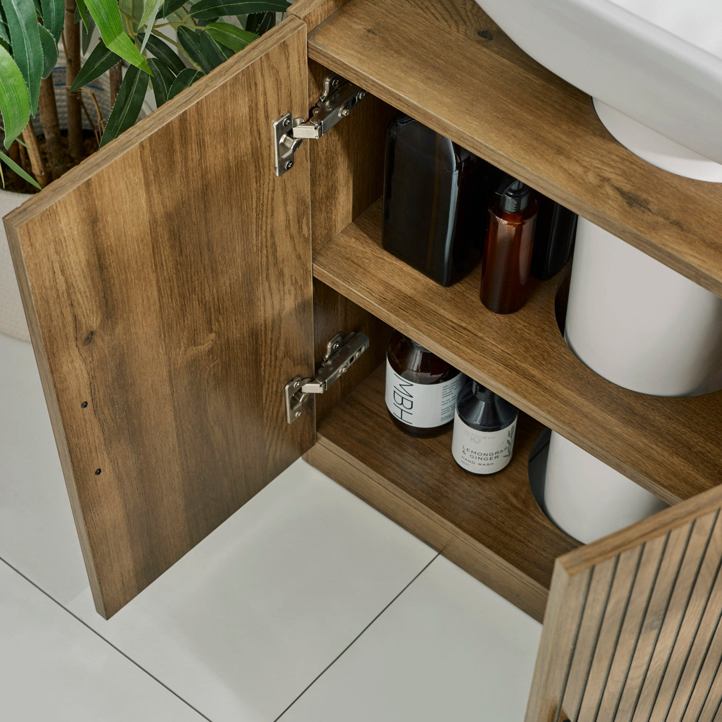 Under sink bathroom unit in brown wood with vertical grooves and black pull handles close-up