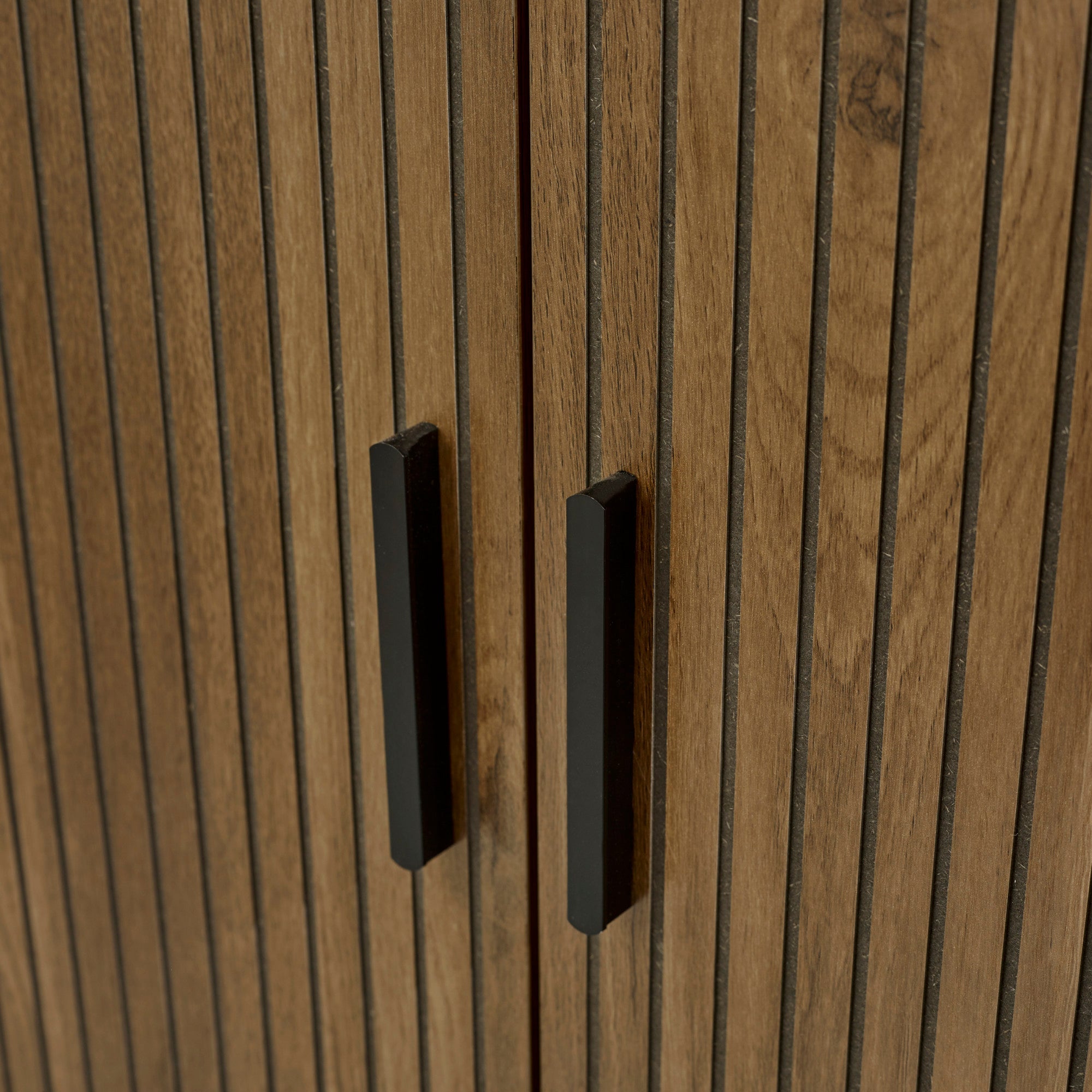 Close-up of black rectangular handles on vertical groove pattern wooden bathroom storage cabinet doors