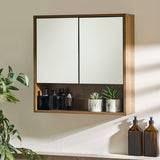 Wall-mounted brown wood bathroom cabinet with two mirrored doors and open shelf holding bottles and plants.
