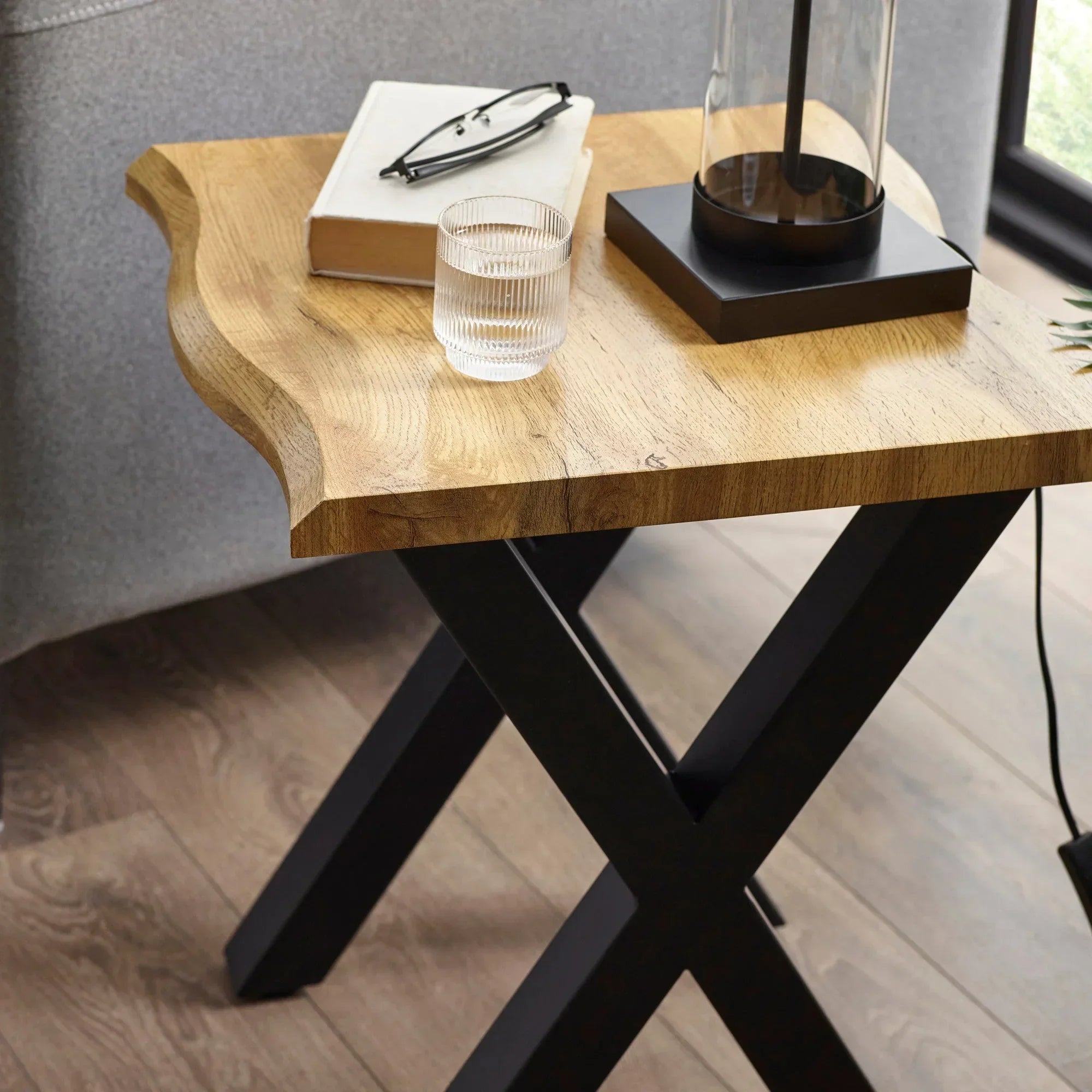 Wood lamp table with X-frame black legs, book, glass of water, and lamp on top