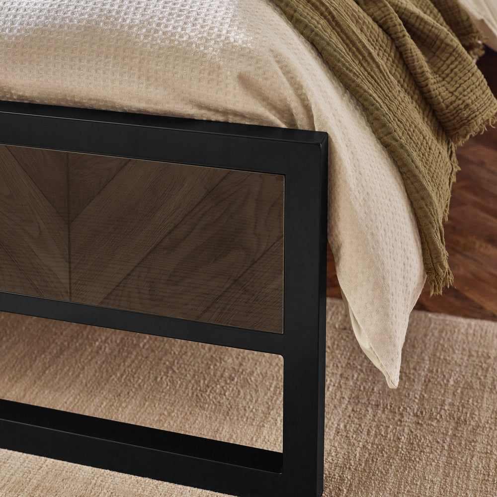 Close-up of bed edge with cream textured bedding and dark wood herringbone patterned headboard