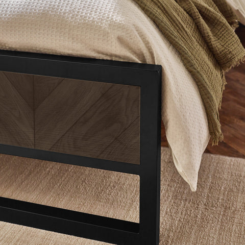 Close-up of bed edge with cream textured bedding and dark wood herringbone patterned headboard