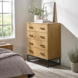 Oak chest of drawers with metal handles and black frame in a modern bedroom setting