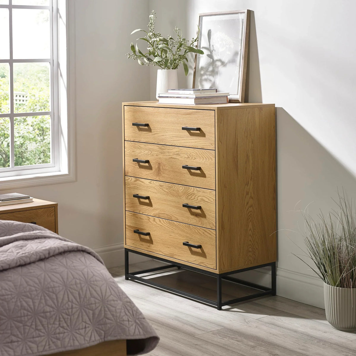 Oak chest of drawers with metal handles and black frame in a modern bedroom setting