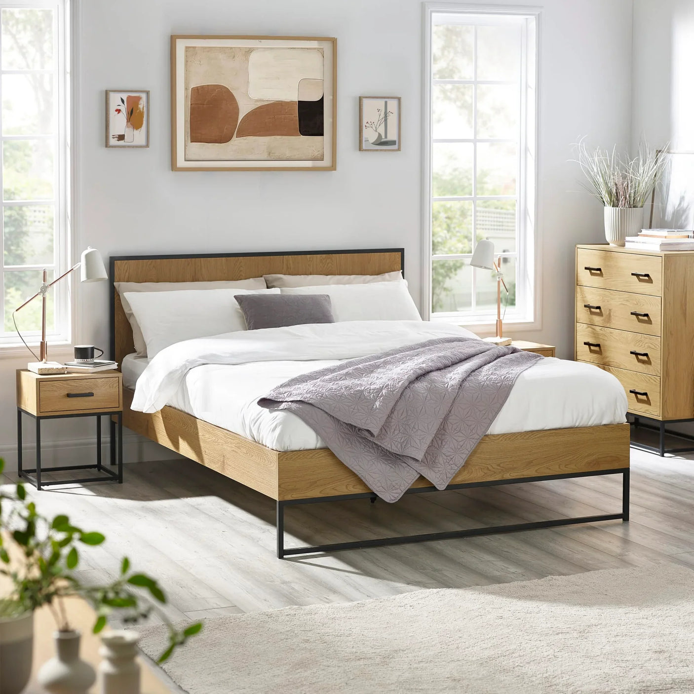 Modern oak bed frame with metal legs in bright bedroom, matching nightstand and chest