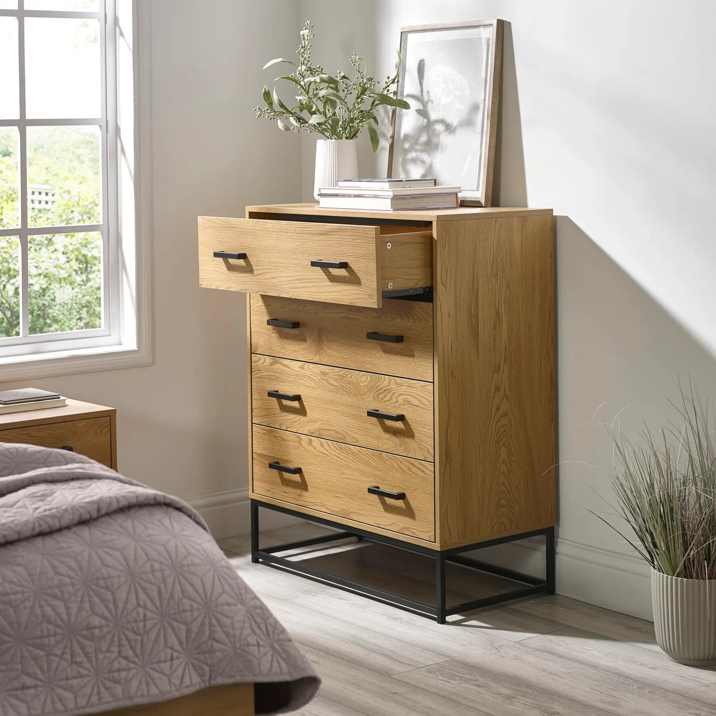 Oak chest of drawers with black metal handles, top drawer open, in modern bedroom