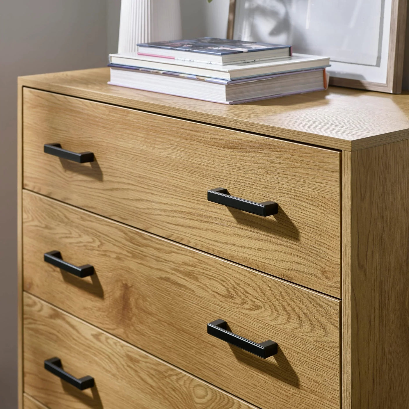Oak chest of drawers with black handles and books stacked on top surface