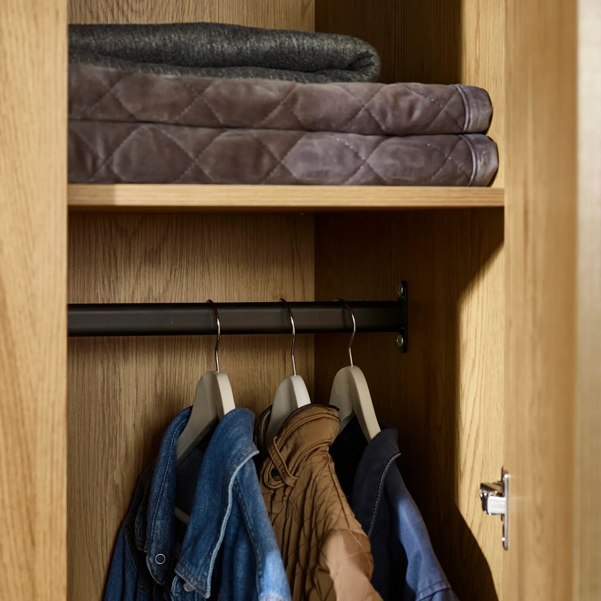 Oak wardrobe interior with clothes rail, jackets on hangers and blankets on shelf