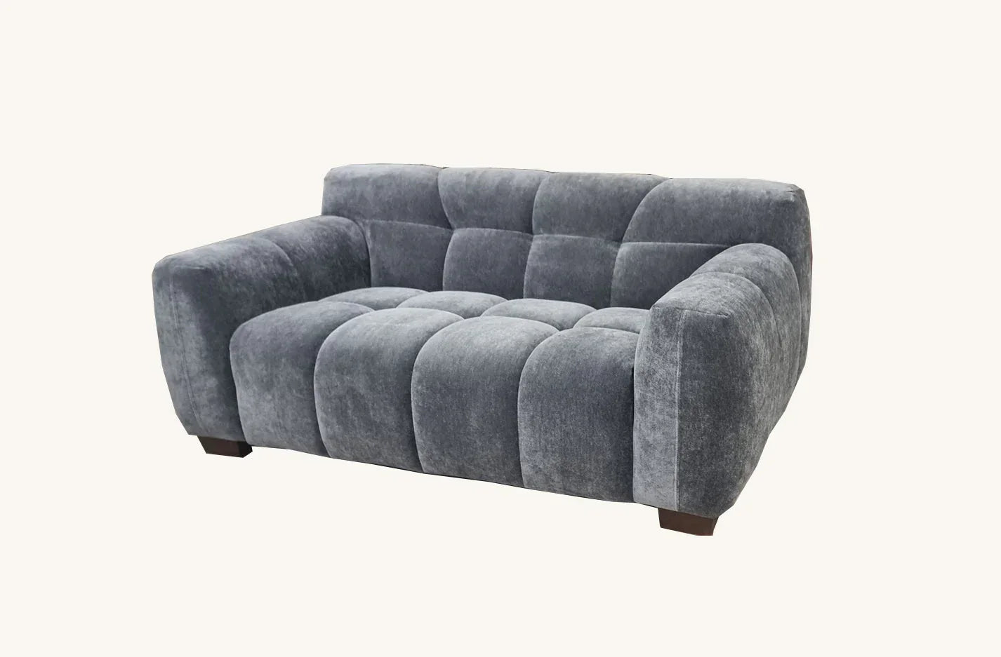 Grey velvet sofa with deep channel tufting and wide arms on a white background