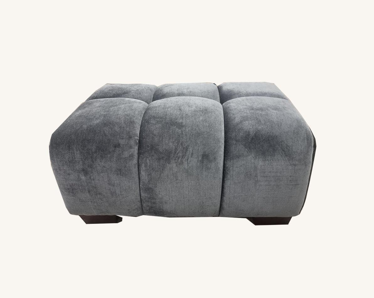Grey velvet upholstered stool with tufted top and short dark wooden legs, front view