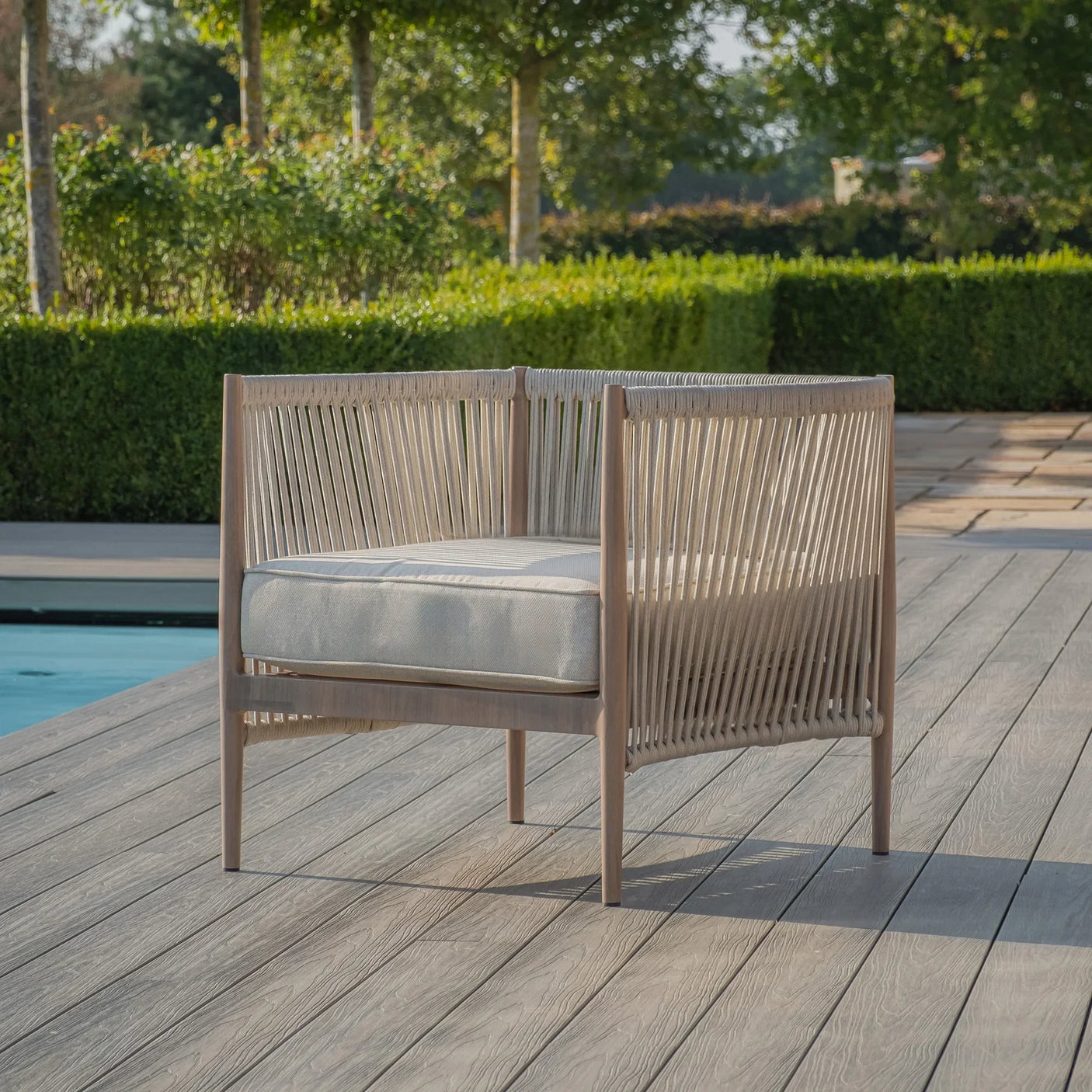 Outdoor rope accent chair with light cushion on decking by a poolside garden