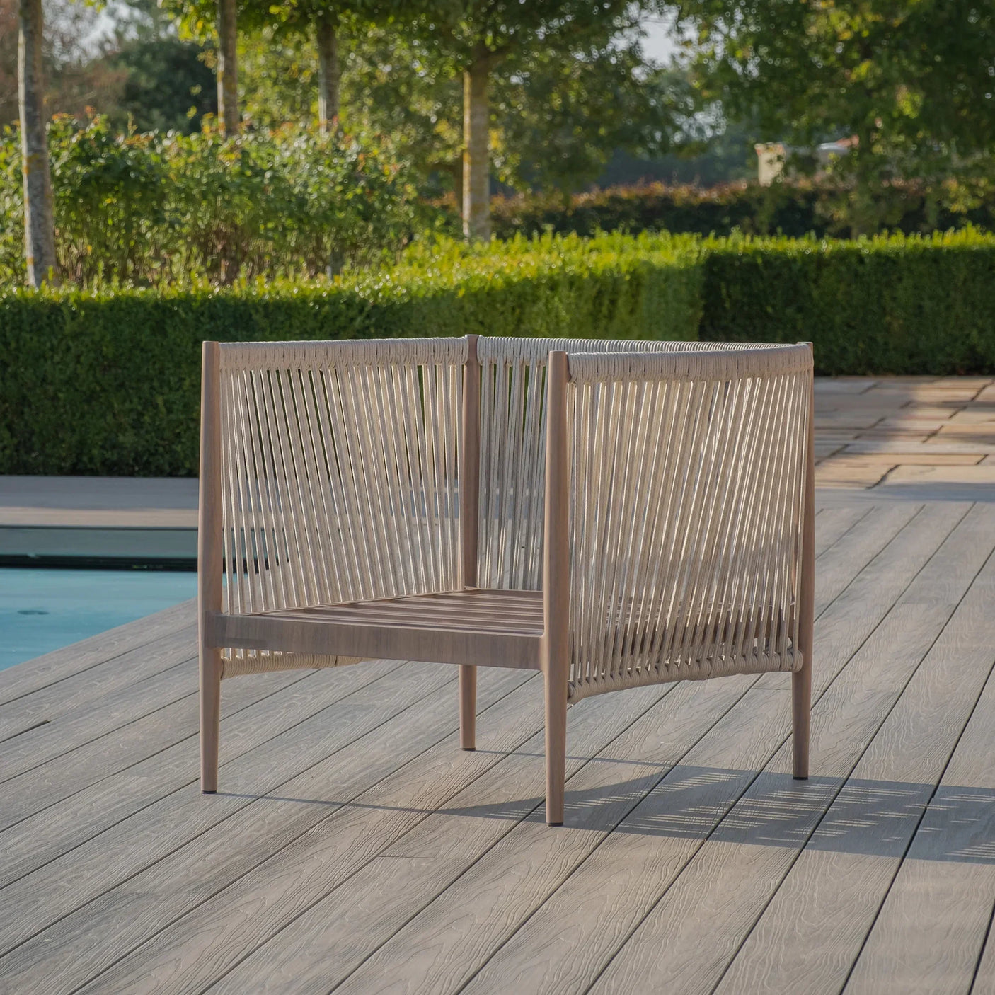 Outdoor rope lounge chair with wooden frame on decking beside garden and pool