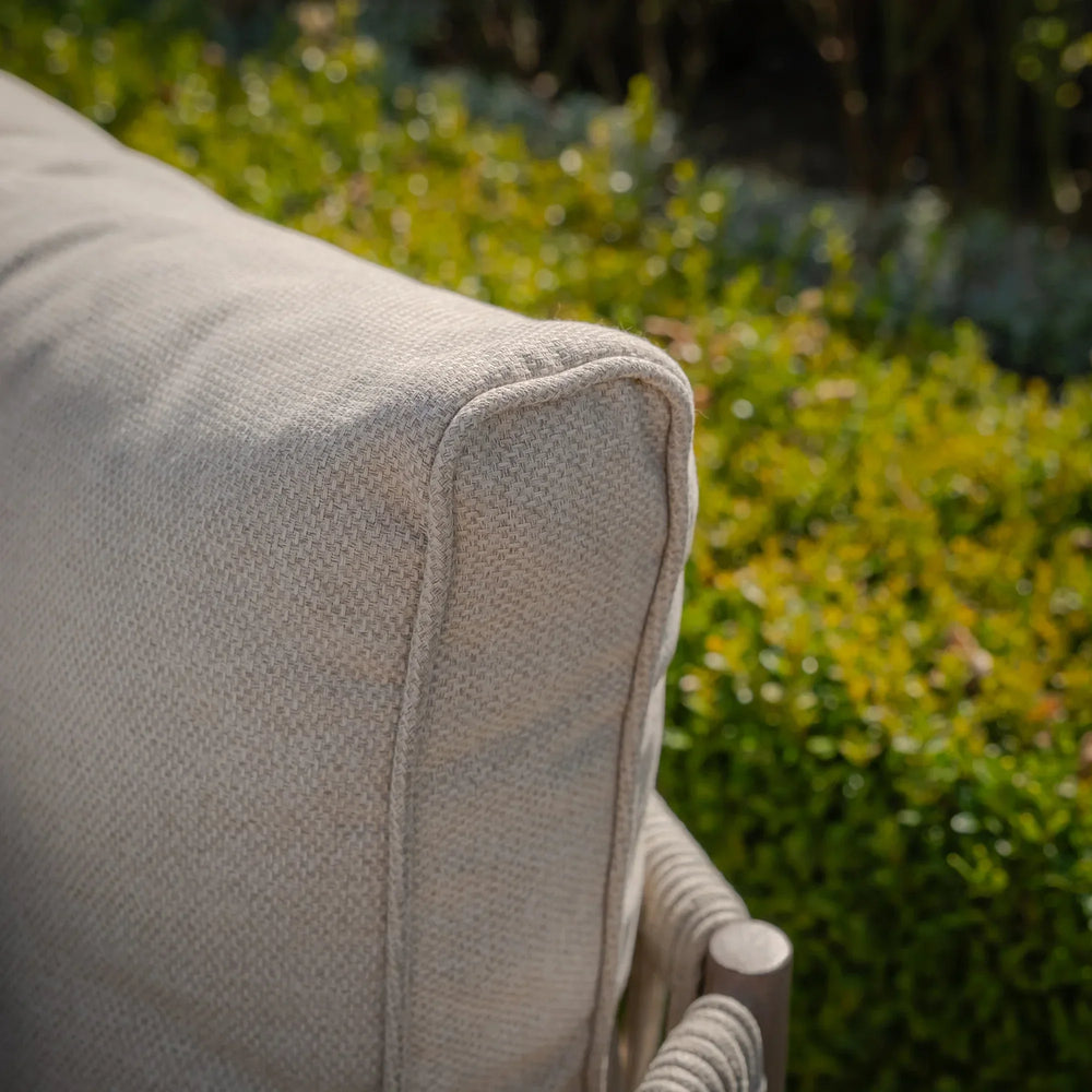 Close-up of outdoor sofa cushion in beige textured fabric with greenery background