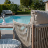 Beige rope outdoor sofa with cushion by pool and patterned round ottoman