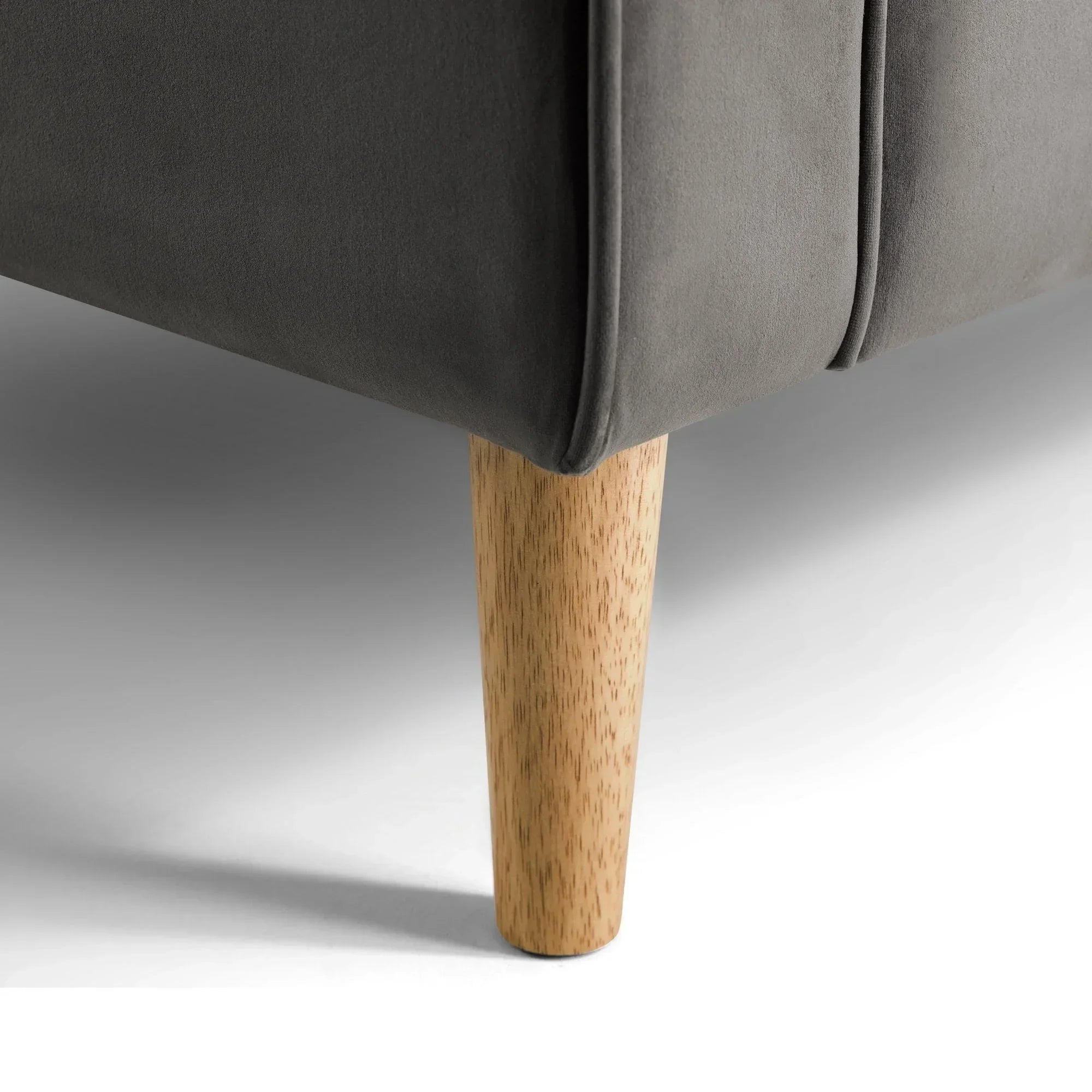 Closeup of grey sofa corner with wooden tapered leg on white floor