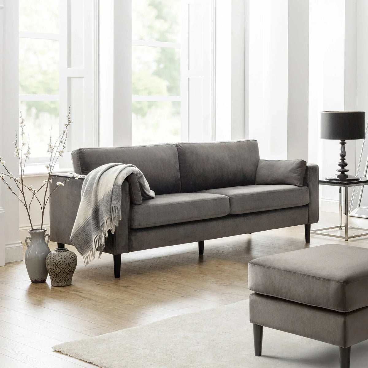 Grey three seater sofa with wooden legs in a bright living room, throw blanket on armrest