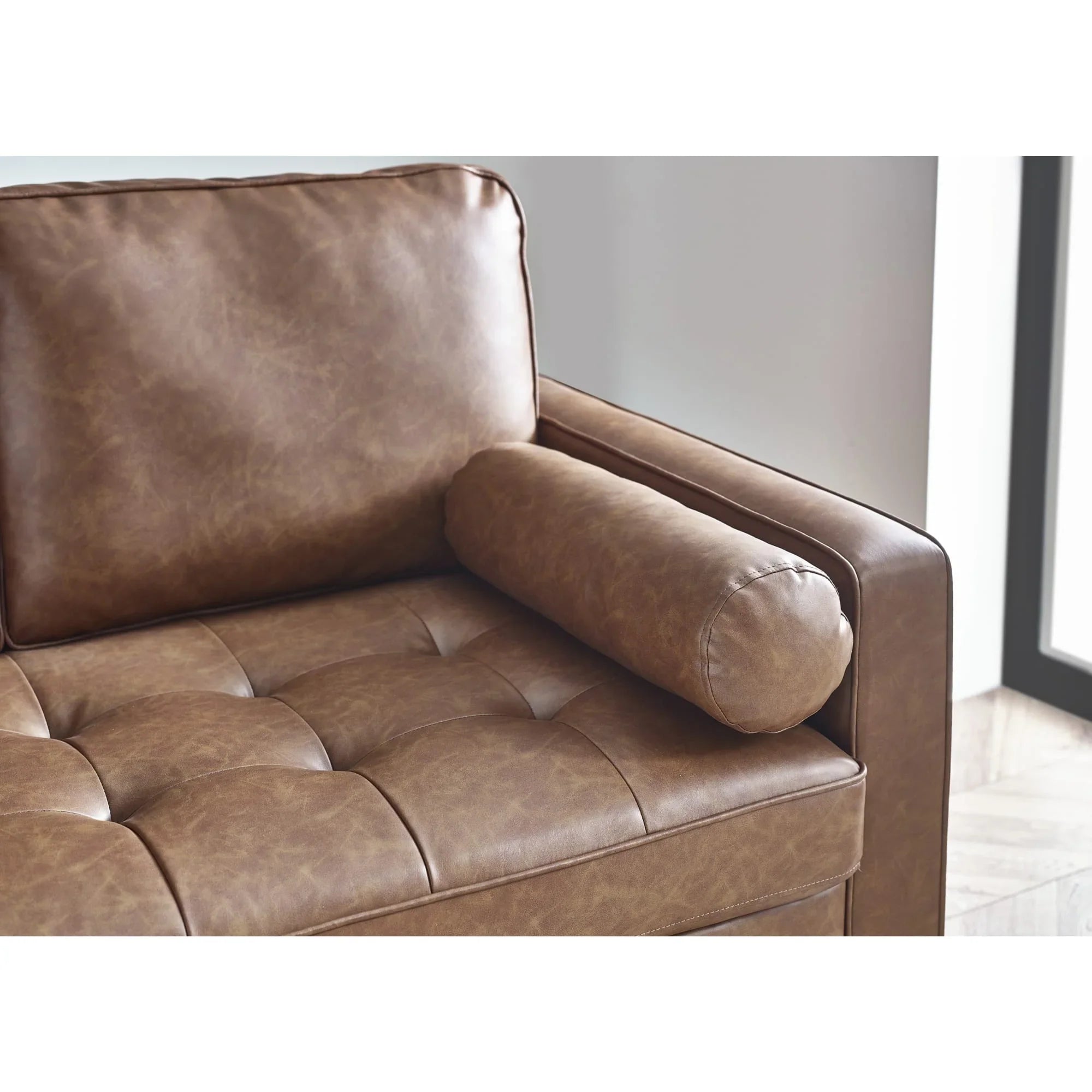 Brown leather sofa armrest with bolstered cushion and tufted seat closeup