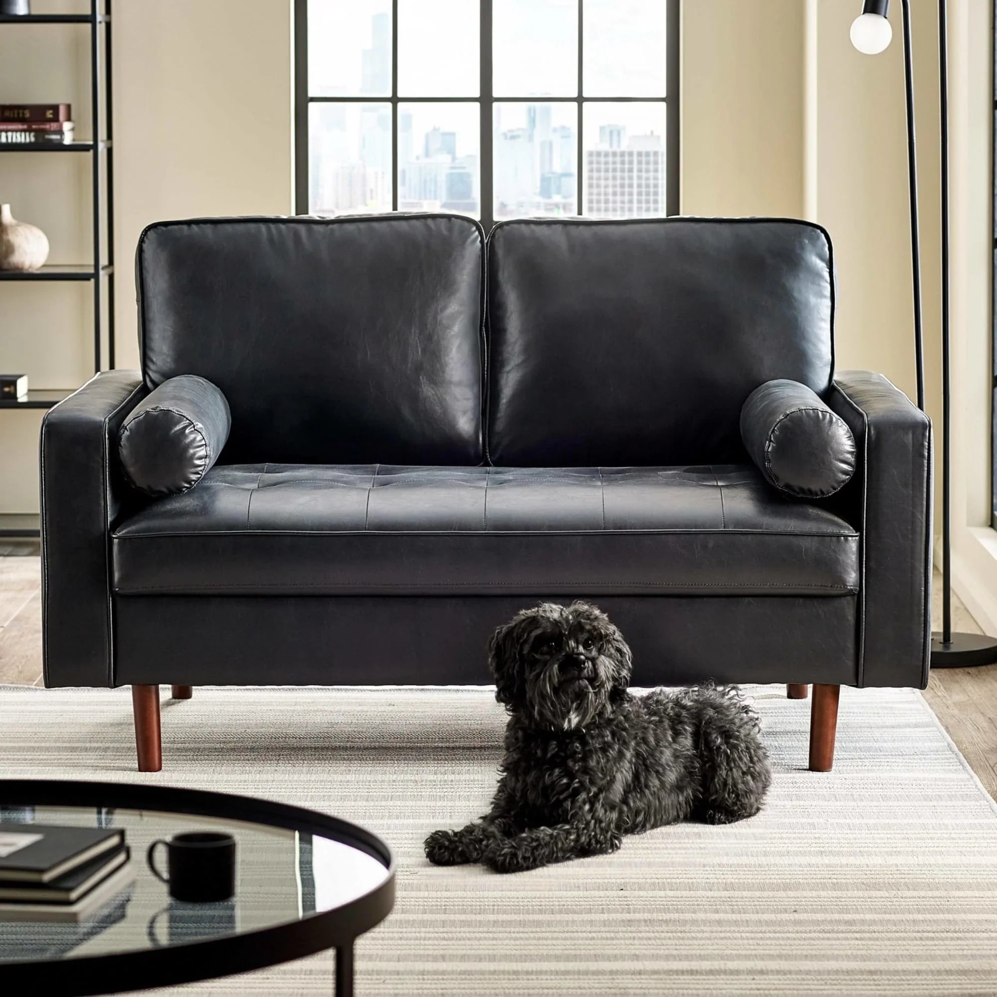 Black leather sofa with round bolster cushions in modern living room, dog on striped rug
