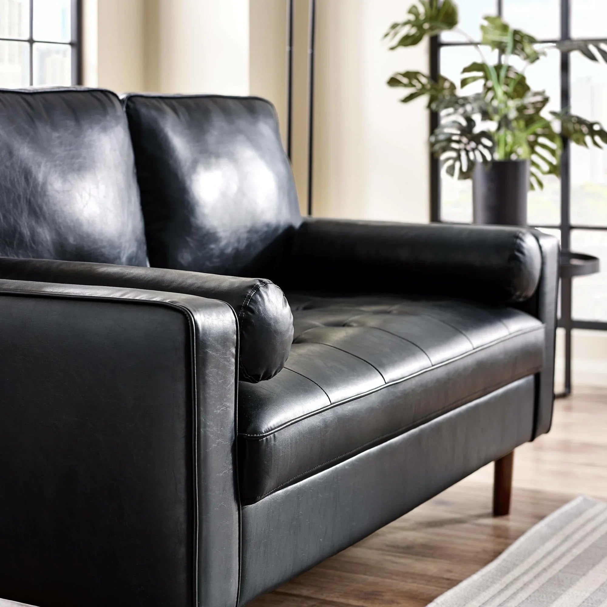 Black leather sofa with tufted seat and wooden legs in modern living room setting