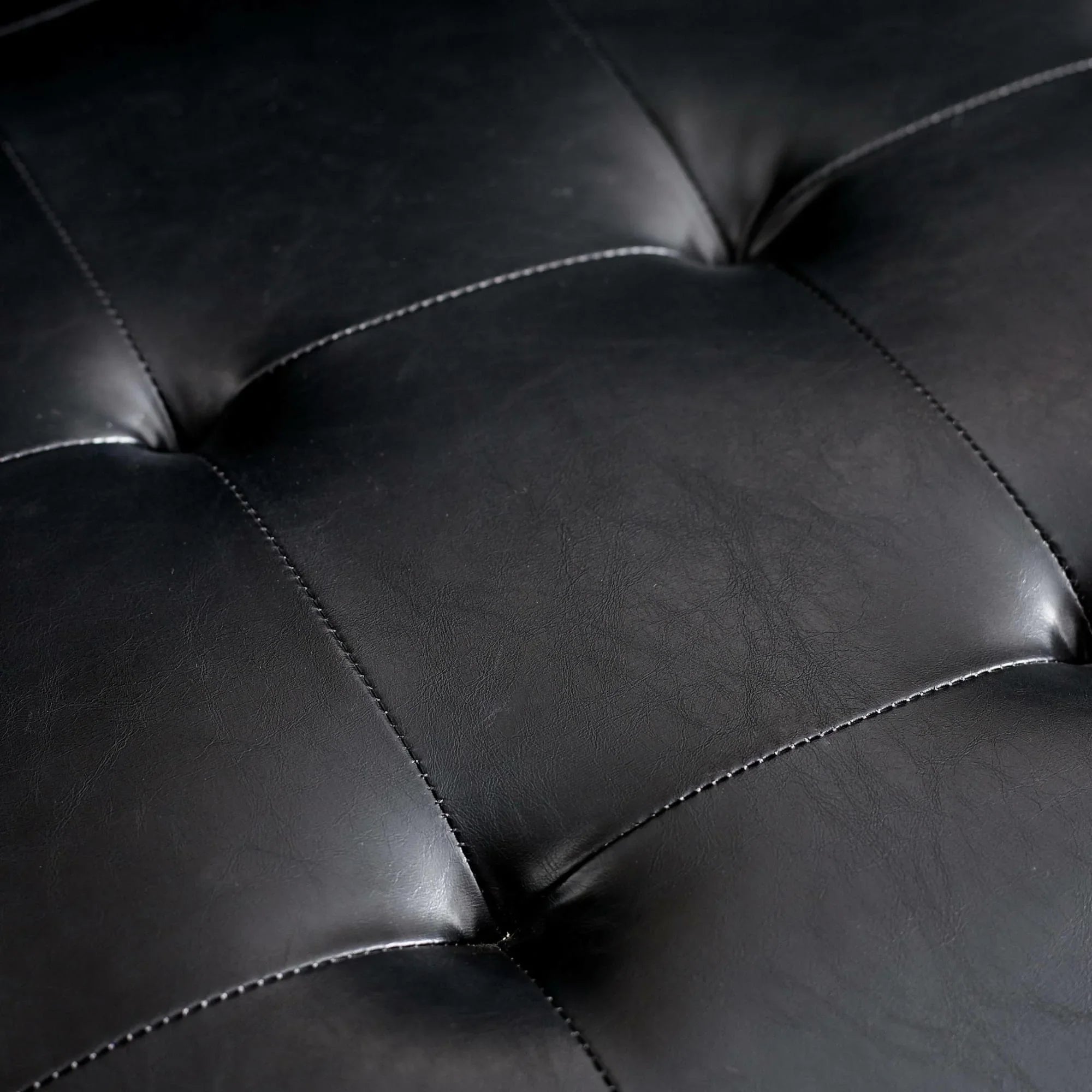 Closeup of black leather sofa cushion with detailed stitching and tufted design