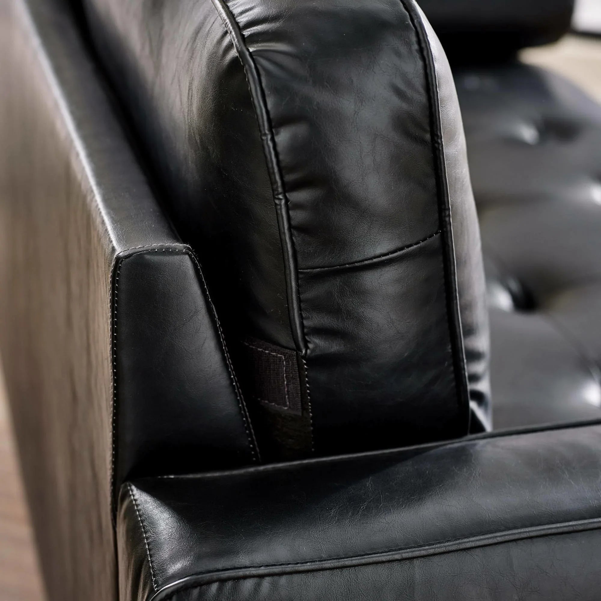 Close view of black leather sofa cushion and stitched armrest